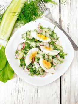 Salad from radish, cucumber, sorrel, greens and eggs, dressed with mayonnaise and sour cream in a plate on the background of wooden boards from above
