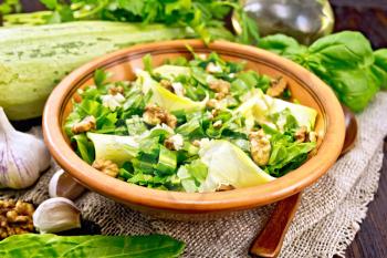 Salad of young zucchini, sorrel, garlic and nuts, seasoned with vegetable oil in clay plate on napkin of sackcloth on a wooden board background