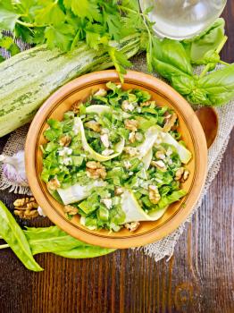 Salad of young zucchini, sorrel, garlic and nuts, seasoned vegetable oil in a plate on napkin of sackcloth on wooden board background from above