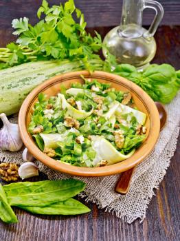 Salad of young zucchini, sorrel, garlic and nuts, seasoned vegetable oil in a plate on napkin of sackcloth on wooden board background