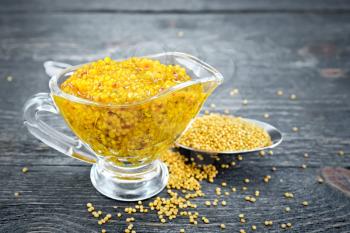 Mustard Dijon sauce in a glass sauceboat and mustard seeds in a spoon on a wooden board background