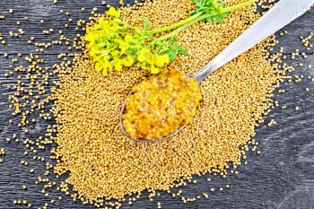Mustard Dijon sauce in a metal spoon and yellow mustard flower on the seeds against a wooden plank top