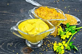 Mustard sauce and Dijon mustard in two glass saucepans, yellow flower and seeds in a spoon on wooden plank background