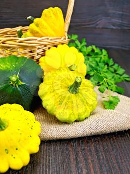 Yellow and green squash on sackcloth and wicker basket, a bunch of parsley on background wooden table