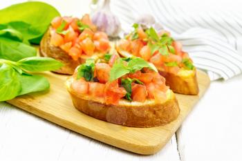 Bruschetta with tomato, basil and spinach on a plate, fresh spinach leaves, napkin and vegetable oil in a decanter on wooden board background