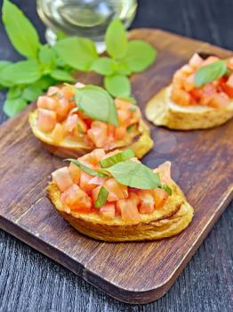 Bruschetta with tomatoes and basil on a dark wooden board background