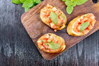 Bruschetta with tomatoes and basil on a dark wooden background from above