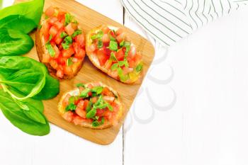 Bruschetta with tomato, basil and spinach on a plate, fresh spinach leaves, napkin and vegetable oil in a decanter on wooden background from above. Text space