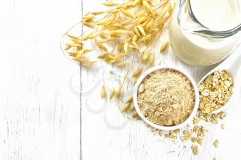 Flour oat in bowl, milk in a jug, oatmeal in spoon, oaten stalks on wooden board background from above
