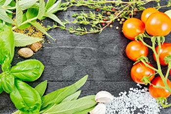 Frame of savory leaves, sage, basil and thyme, salt, nutmeg and garlic, mustard seeds, peas and tomatoes on the background of wooden boards