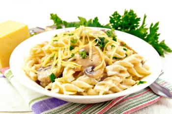 Fusilli pasta with mushrooms in creamy sauce, parsley and grated cheese in a dish on towel on wooden board background
