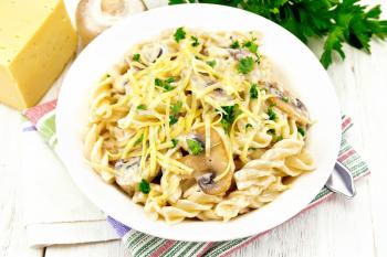 Fusilli pasta with mushrooms in creamy sauce, parsley and grated cheese in a plate on towel against light wooden board