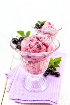 Ice cream with black currant in two glasses on a lilac napkin, berries with leaves against a light wooden board
