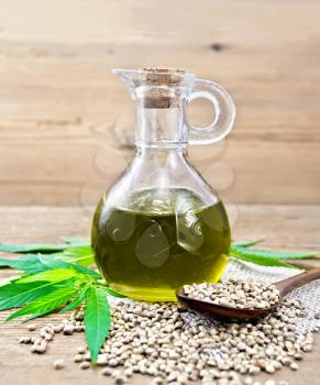 Hemp oil in a glass decanter, grain in a spoon and on the table, cannabis leaves on a wooden board background