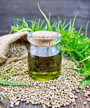 Hemp oil in a glass jar, grain in a bag and on the table, leaves and stalks of cannabis against a dark wooden board