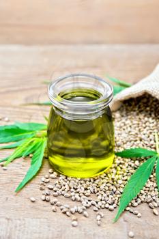 Hemp oil in a glass jar, grain in a bag and on the table, cannabis leaves on the background of an old wooden board