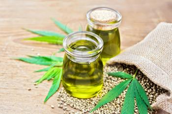 Hemp oil in two glass jars, grain in the bag and on the table, cannabis leaves on the background of an old wooden board
