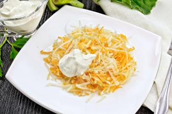 Salad of fresh carrots and kohlrabi cabbage with sour cream in a plate, napkin and fork on a wooden plank background
