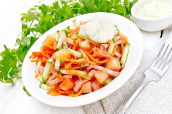 Salad from smoked sausage, spicy carrot, tomato, cucumber and spices with mayonnaise, napkin, fork and parsley on a wooden board background