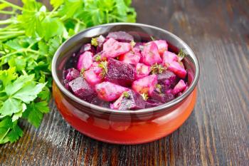Beetroot and potato salad, seasoned with vegetable oil and vinegar in a bowl, parsley against a dark wooden board