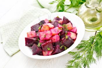 Beetroot and potato salad, seasoned with vegetable oil and vinegar in a plate, napkin, parsley and dill on a wooden board background