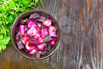 Beetroot and potato salad, seasoned with vegetable oil and vinegar in a bowl, parsley on a wooden board background from above