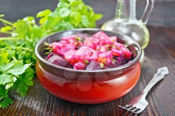 Beetroot and potato salad, seasoned with vegetable oil and vinegar in a bowl, parsley and fork on a dark wooden board background