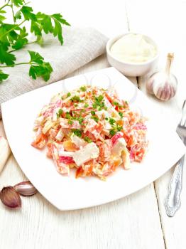 Salad of crab sticks, cheese, garlic and tomatoes, filled with mayonnaise, kitchen towel and parsley on a wooden board background
