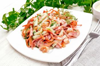 Salad from smoked sausage, spicy carrot, tomato, cucumber and spices, dressed with mayonnaise, napkin, fork and parsley on a light board background