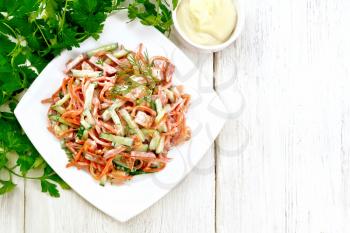 Salad from smoked sausage, spicy carrot, tomato, cucumber and spices, dressed with mayonnaise, towel, fork and parsley on a wooden board background from above