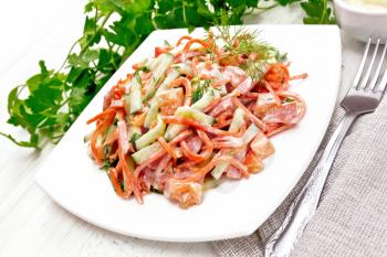 Salad from smoked sausage, spicy carrot, tomato, cucumber and spices, dressed with mayonnaise, towel, fork and parsley against the background of a light board