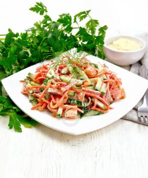 Salad from smoked sausage, spicy carrot, tomato, cucumber and spices, dressed with mayonnaise, napkin, fork and parsley on a wooden board background