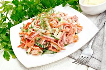 Salad from smoked sausage, spicy carrot, tomato, cucumber and spices, dressed with mayonnaise, napkin, fork and parsley on a light wooden board background