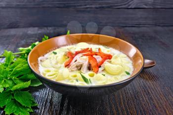 Soup from chicken meat, pasta with cream and sweet pepper, parsley and cilantro in a clay plate on a wooden board background