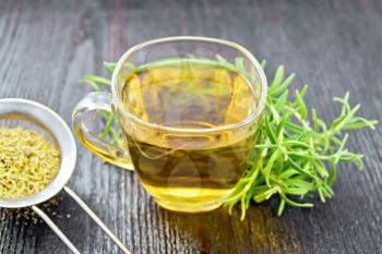 Rosemary herbal tea in a cup, a strainer with dry herb on a wooden board background
