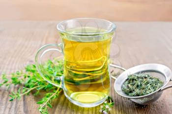 Herbal tea in a glass mug of thyme, metal strainer with dry leaves, a bunch of fresh savory on a wooden board background