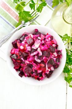 Vinaigrette salad with pickled or sauerkraut, potatoes, beetroot and onion, seasoned with vegetable oil in a bowl, napkin, parsley on the background of a light wooden board on top