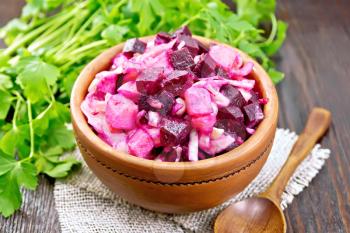 Vinaigrette salad with pickled or sauerkraut, potatoes, beetroot and onion, seasoned with vegetable oil in a bowl on burlap, parsley, spoon on a wooden board background