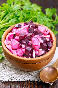 Vinaigrette salad with pickled or sauerkraut, potatoes, beetroot and onions, seasoned with vegetable oil in a clay bowl on burlap, parsley against a dark wooden board