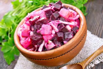 Vinaigrette salad with pickled or sauerkraut, potatoes, beetroot and onions, seasoned with vegetable oil in a clay bowl on burlap, parsley on a wooden board background
