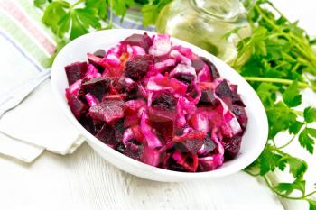 Vinaigrette salad with pickled or sauerkraut, potatoes, beetroot and onion, seasoned with vegetable oil in a bowl, towel, parsley on the background of a light wooden board