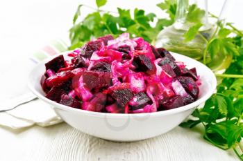 Vinaigrette salad with pickled or sauerkraut, potatoes, beetroot and onion, seasoned with vegetable oil in a bowl, towel, parsley on a wooden board background