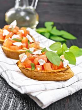 Bruschetta with tomato, basil and soft cheese on a napkin on wooden board