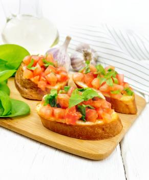 Bruschetta with tomato, basil and spinach on a plate, fresh spinach leaves, napkin and vegetable oil in a decanter against white wooden board