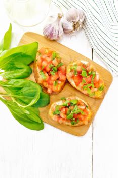 Bruschetta with tomato, basil and spinach on a plate, fresh spinach leaves, napkin and vegetable oil in a decanter against light wooden board from above
