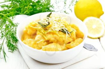 Pumpkin gnocchi with sage, lemon, cheese and butter in a bowl on a towel against the background of light wooden board