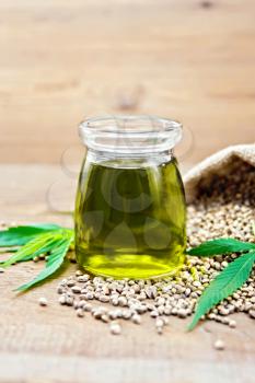 Hemp oil in a glass jar, grain in a bag and on the table, cannabis leaves on a wooden board background