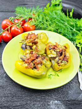 Pepper stuffed with mushrooms, tomatoes, zucchini, eggplant and onions, seasoned with wine, garlic, thyme and spices in a green plate, fork, parsley on wooden board background