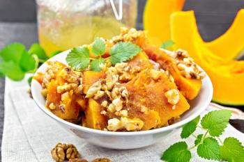 Pumpkin with walnuts and honey in a bowl on a towel, mint and fork on the background of wooden boards