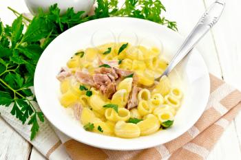 Soup from chicken meat, pasta with cream and cilantro in a plate on a towel, parsley, metal spoon on the background of a light wooden board
